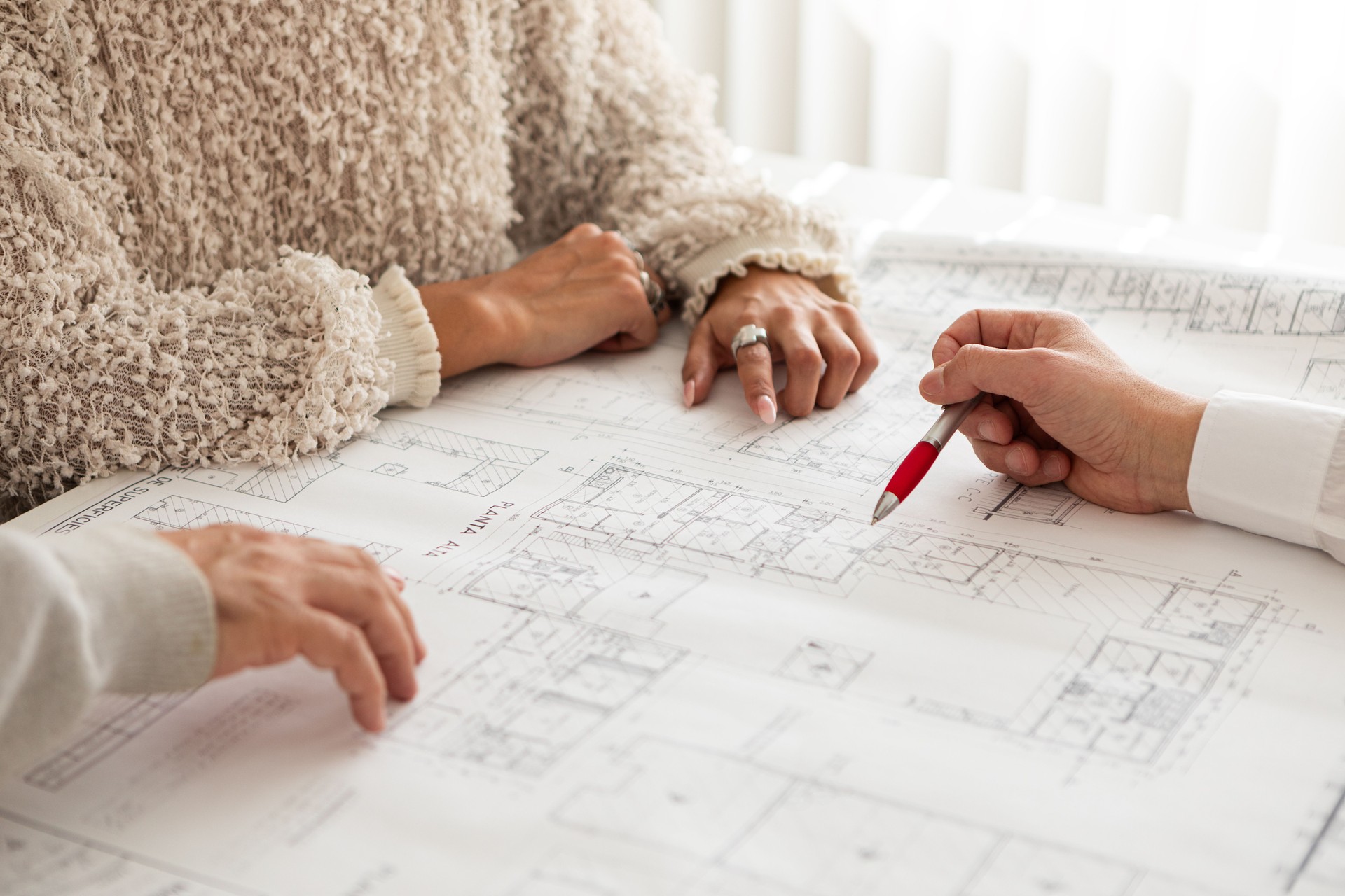 Closeup of male hand pointing at an architectural plan to clients